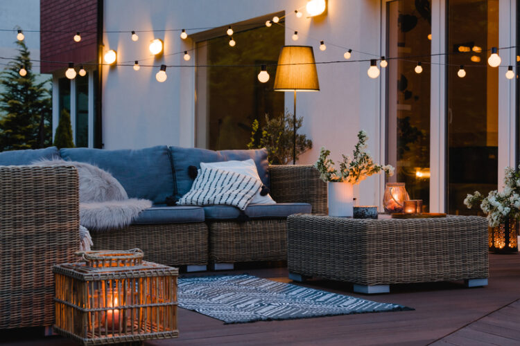 Wicker furniture on a deck at dusk with string lights.